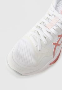 Scarpa atletica bianca con tomaia in tessuto testurizzato, dettagli rosa e lacci bianchi. Punta arrotondata e suola imbottita per supporto.