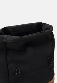Sac à dos noir et marron avec le haut ouvert, comportant deux clips de boucle noirs et une bande de Velcro à l'intérieur de l'ouverture.