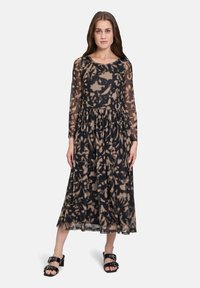 Langes schwarzes Kleid mit transparenten langen Ärmeln, das ein beiges abstraktes Blumenmuster, einen runden Ausschnitt und einen ausgestellten Saum hat.