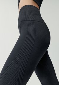 Čierne legíny s textúrovaným ryhovaním, so zvýšeným pásom a priliehajúcim strihom, zdôrazňujúce atletickú funkčnosť a podporu.