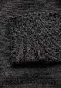 Schwarzer Textilstoff mit einer zerknitterten Struktur, der eine Falte zeigt, die die Tiefe und das Material verdeutlicht. Die Oberfläche erscheint weich und leicht reflektierend.