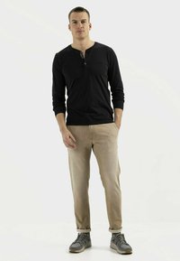 Schwarz langärmliges Henley-Shirt mit Knopfleiste, kombiniert mit hellbeigen Hosen und grauen Sportschuhen.