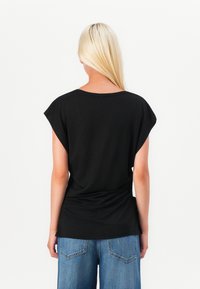 Top nero a maniche corte con vestibilità morbida, scollatura rotonda e dettaglio arricciato sul retro, abbinato a jeans in denim a gamba larga blu chiaro.