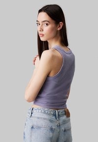 Top in lilac a costine con scollatura tonda, design aderente e senza maniche, abbinato a jeans azzurri a vita alta.