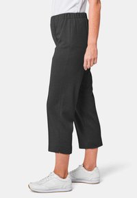 Zwarte cropped broeken met een elastische tailleband, met een rechte pijp en zijsplitsen aan de zoom. Draagt u met witte sneakers.