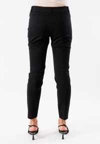 Pantaloni neri su misura realizzati in tessuto elasticizzato, con una vestibilità slim, vita piatta e tasche laterali. Texture liscia, lunghezza alla caviglia.