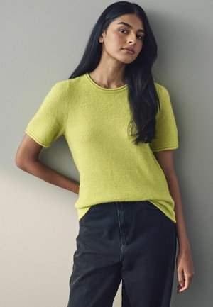 Bright yellow knit top with short sleeves and a rounded neckline, paired with dark denim pants. Soft texture, relaxed fit, and minimal detailing.