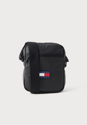 Borsa a tracolla nera con tasca frontale con cerniera, tracolla regolabile e patch con logo Tommy Jeans in rosso, bianco e blu al centro della parte anteriore.