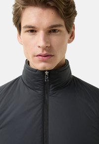 Czarna pikowana kurtka z wysokim kołnierzem, zamkiem błyskawicznym i gładką, lekką fakturą. Bez widocznych wzorów ani akcentów. Dopasowany fason.