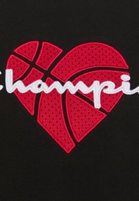 Tissu noir avec un cœur rouge orné de coutures de basket-ball et le mot « champion » brodé en cursive blanche.