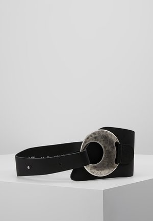 Ceinture en cuir noir avec un design large et une grande boucle ronde texturée en argent reposant sur une surface blanche.