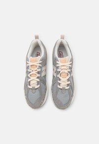 Šedé sportovní tenisky s textilem z prodyšné síťoviny, krémovými tkaničkami, kontrastními akcenty a gumovou podešví, vybavené poutkem na patě pro snadné obouvání.