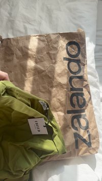 Groene kleding in zachte stof met een label "EDITED," gelegen op een gekreukt bruin papieren zakje gemarkeerd "zalando." Lichte achtergrond.
