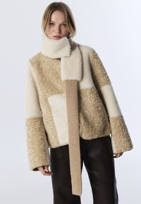 Faux fur jack in beige en roomkleur, met een gestructureerd patchworkontwerp en een lange, geribde sjaal in een bijpassende kleur.