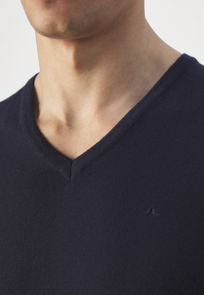 Pull à col en V bleu marine réalisé en maille douce. Doté d'un logo discret sur la poitrine et d'une texture lisse. L'encolure est bien définie.