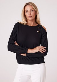 Czarny, prążkowany, długi top z długim rękawem, charakteryzujący się fasonem odsłaniającym ramiona oraz dyskretnym złotym zapięciem na lewym ramieniu.