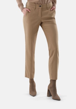 Pantaloni beige su misura con vestibilità slim, dotati di tasche laterali, chiusura frontale con bottone e una texture liscia, abbinati a stivali con tacco dello stesso colore.