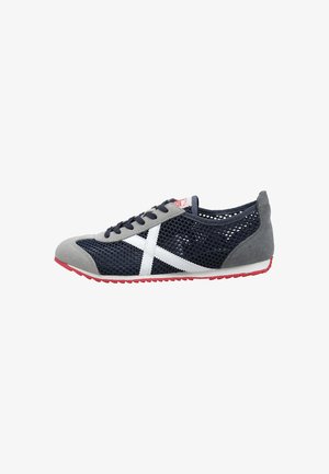 Baskets en mesh bleu marine avec bout et talon en daim gris, détail blanc en forme de croix sur le côté, lacets noirs et semelle en caoutchouc rouge.