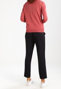 Suéter rosa con detalles de encaje en los hombros, combinado con pantalones negros y zapatillas blancas. El conjunto enfatiza un estilo casual y cómodo.