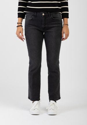 Jeans neri in denim con taglio dritto, tasche anteriori e chiusura con bottone, abbinati a sneakers bianche su uno sfondo neutro.