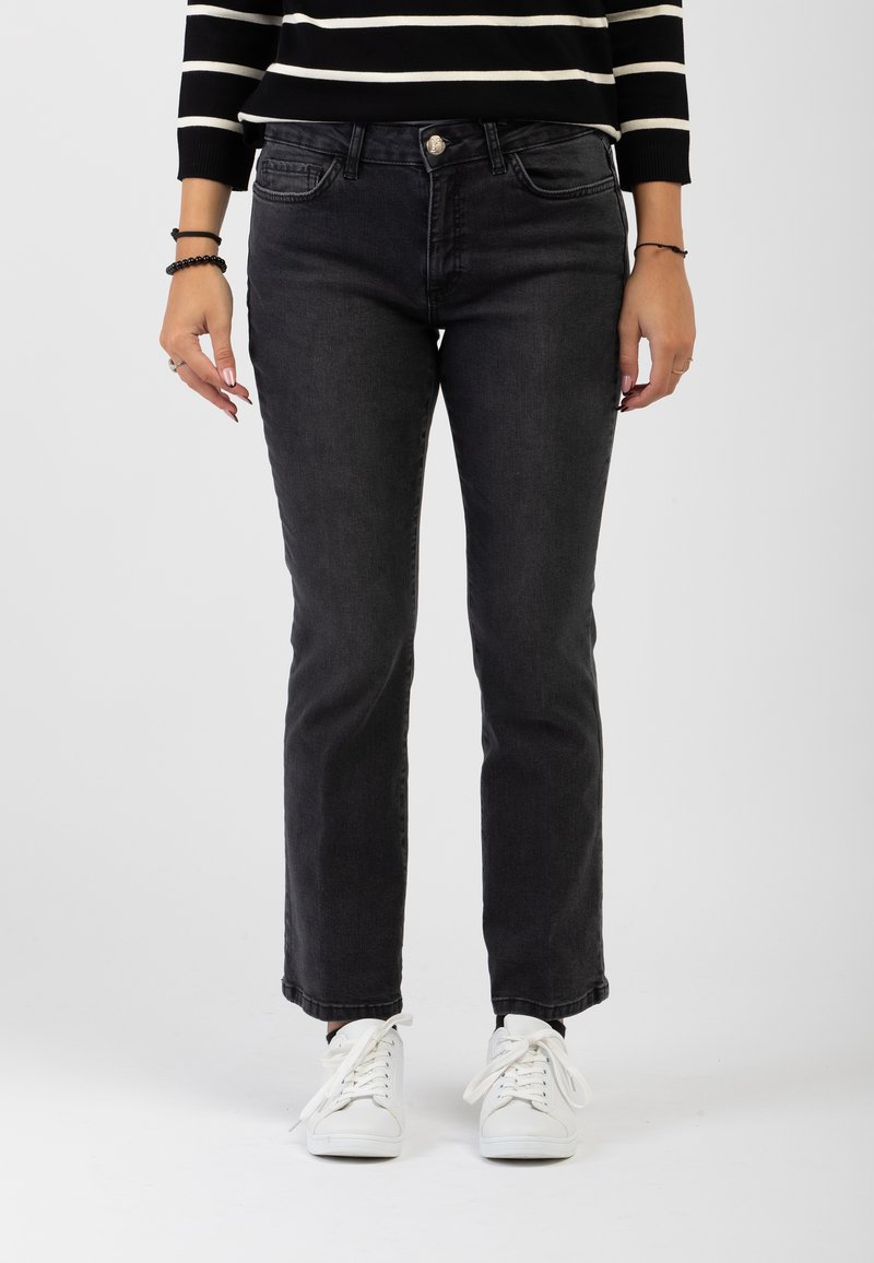 Jeans neri in denim con taglio dritto, tasche anteriori e chiusura con bottone, abbinati a sneakers bianche su uno sfondo neutro.