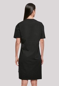 Schwarzes Baumwoll-T-Shirt-Kleid mit kurzen Ärmeln, lockerer Passform und mittellangem Design. Verfügt über einen geraden Saum und subtile Rückennahtdetails.