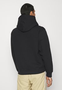 Svart hoodie med avslappnad passform, mjukt material, ribbade ärmar och nederkant, samt en minimalistisk design utan synliga logotyper.