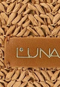 Fibras naturales tejidas crean una superficie texturizada de color marrón claro, acentuada por una etiqueta de cuero color tostado con la palabra "LUNA" en dorado metálico.