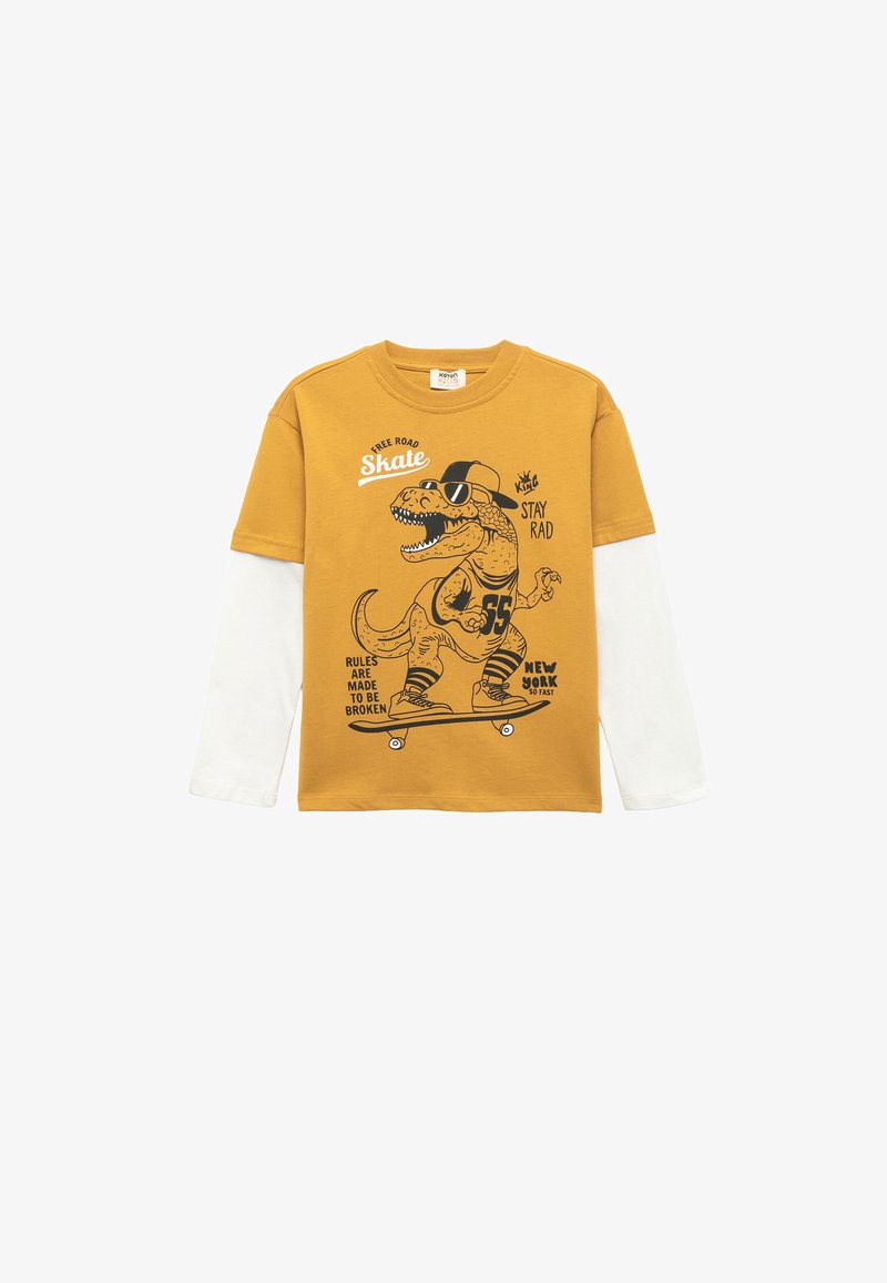 T-shirt à manches longues jaune avec une couche inférieure blanche présentant un graphique de dinosaure noir, un skateboard et des éléments de texte en noir.