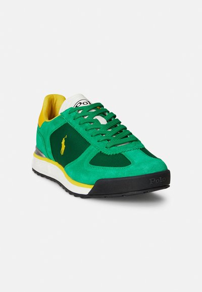 Green and yellow athletic sneaker with suede and mesh materials. Features a logo, lace-up design, and a textured black rubber sole.
