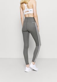 Leggings grigi con strisce laterali bianche, vita alta e tessuto elasticizzato. Abbinati a un reggiseno sportivo bianco con spalline incrociate e dettaglio a taglio.
