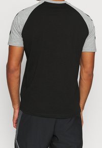Sort og grå kortærmet T-shirt med raglanærmer. Kroppen er sort, og ærmerne er lys grå. Blødt stof.