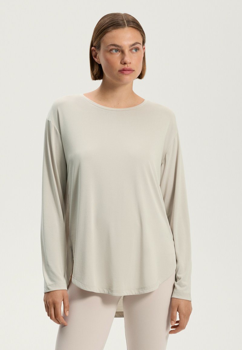 Top beige a maniche lunghe con scollatura rotonda, texture morbida e orlo curvo. Presenta una vestibilità ampia e spacchi laterali per facilitare i movimenti.
