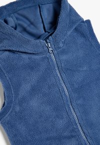 Gilet in pile blu con zip frontale, cappuccio e texture morbida. Presenta una fodera interna liscia e dettagli di cucitura in evidenza.