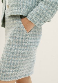 Giacca tweed blu chiaro e bianca con un modello a spina di pesce testurizzato, caratterizzata da una silhouette aderente e dettagli con tasche laterali.