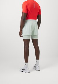 Conjunto deportivo masculino que incluye una camiseta ajustada de un rojo brillante y pantalones cortos de color verde menta claro sobre pantalones cortos de compresión, combinados con zapatillas blancas.