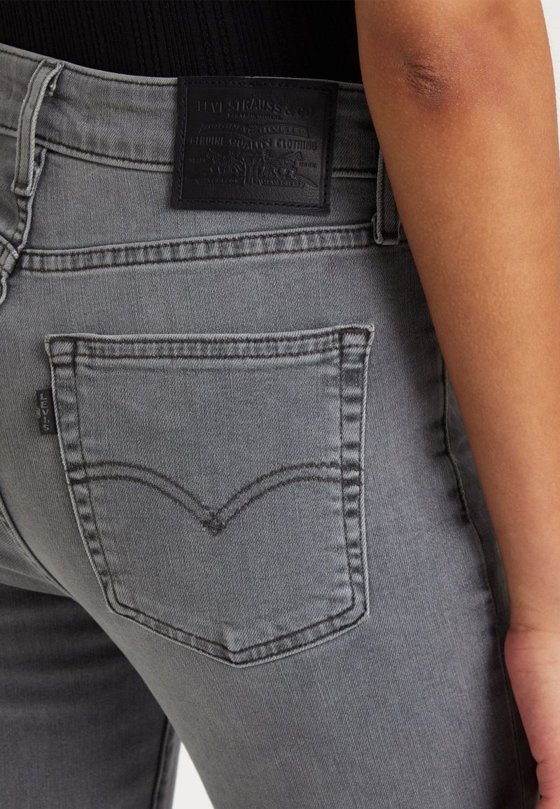 Graue Jeans aus Denim mit einer Gesäßtasche, die mit einem charakteristischen, abgerundeten Stichdesign versehen ist. Lederpatch am Taillenbund mit Markeninformationen.