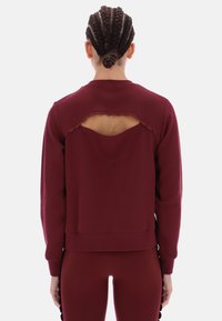 Burgundowa bluza z falowanym wycięciem z tyłu. Miękki, teksturowany materiał i luźny krój z długimi rękawami.