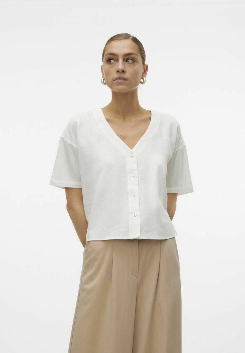 Blusa bianca a maniche corte con scollatura a V e bottoni frontali, realizzata in un tessuto leggero, caratterizzata da una vestibilità comoda e una superficie liscia.