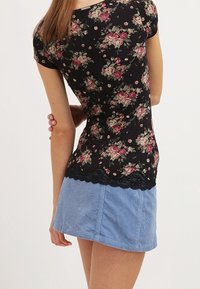 Top negro con flores, de manga corta y con borde de encaje, combinado con una falda de mezclilla azul clara con textura de pana y corte recto.