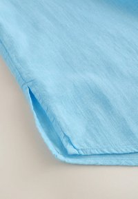 Tissu en lin bleu clair avec une texture douce, présentant un bord net et des détails de couture subtils le long de l'ourlet.