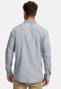 Camisa de manga larga gris claro hecha de una tela suave, con un collar clásico, puños abotonados y un dobladillo recto.