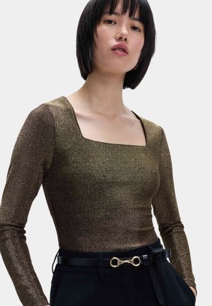 Top de manga larga en tejido metálico bronce con escote cuadrado. Combinado con un pantalón negro con cinturón que presenta un detalle de hardware dorado.