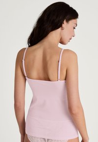 Light pink camisole with thin adjustable straps and a fitted design. Material appears smooth with minimal texture, suitable for layering.
