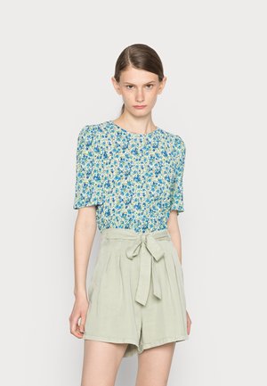 Blusa floral em tons de azul e verde com mangas bufantes curtas, combinada com calções de cintura alta, verde claro, com um cinto de laço.