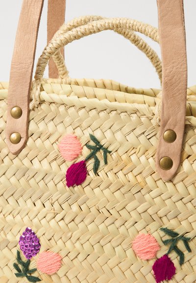 Sac en paille tissé avec des anses en cuir rose pâle. Présente des accents floraux brodés colorés en rose, violet et vert.