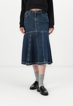 Jeanskjørt med en flagrende silhuett, mørk blå farge, rå kant og midtsemdetaljer. Kombinert med grå sokker og svarte loafers.