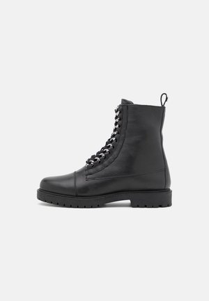 Botte de combat noire en cuir avec semelle épaisse en caoutchouc et languette à l'arrière, vue de profil gauche sur fond blanc.