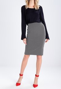 Černý top s dlouhým rukávem v kombinaci s vypasovanou sukni na bílé a černé puntíky. Červené sandály na podpatku s kotníkovými pásky dotvářejí outfitu.