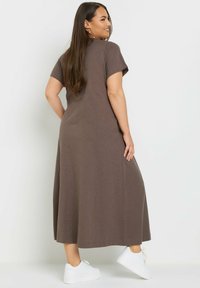 Braunes, knielanges Kleid mit kurzen Ärmeln aus weichem Stoff und schlichter Gestaltung. Kombiniert mit weißen Sneakers und einem lässigen Schnitt.